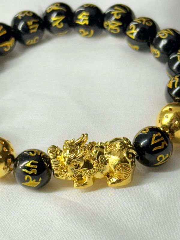 Dark beaded bracelet with gold-coloured lettering and a sculptural detail