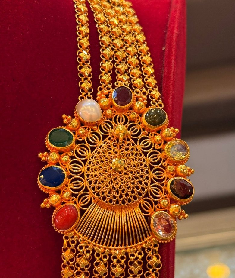Chandrahaar necklace with an intricate round centrepiece and coloured stones on red velvet